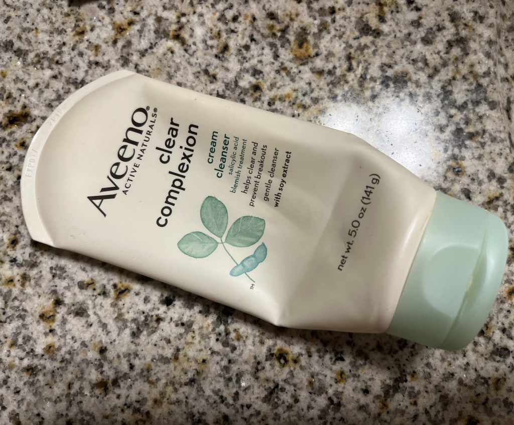 A tube of Aveeno Clear Complexion cream cleanser on a bathroom counter.